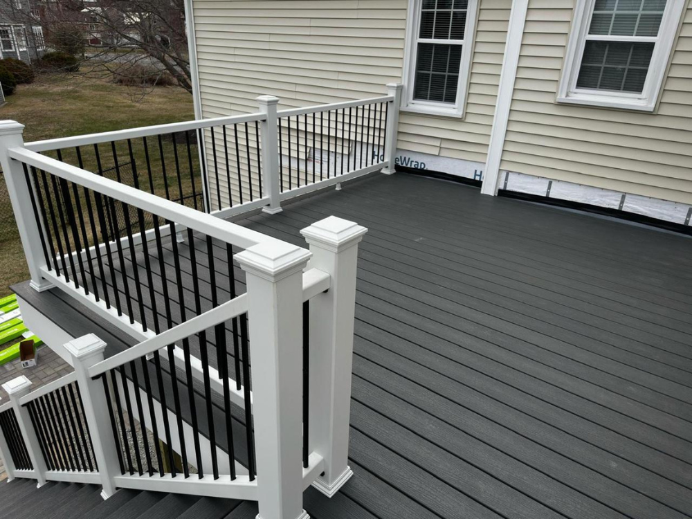 Image of a recently completed Deck Remodeling Project, showcasing a modern composite deck with black metal balusters and white railings, attached to a beige-sided house.
